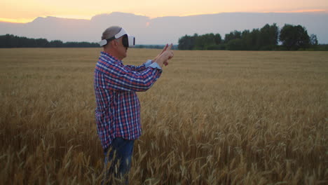 An-elderly-farm-uses-a-VR-helmet-while-standing-in-a-field-at-sunset.-Use-gestures-for-virtual-reality-in-agriculture.